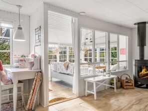 Een gezellige kamer met een witte inrichting, een groot raam, een open haard en een bankje bij het raam.