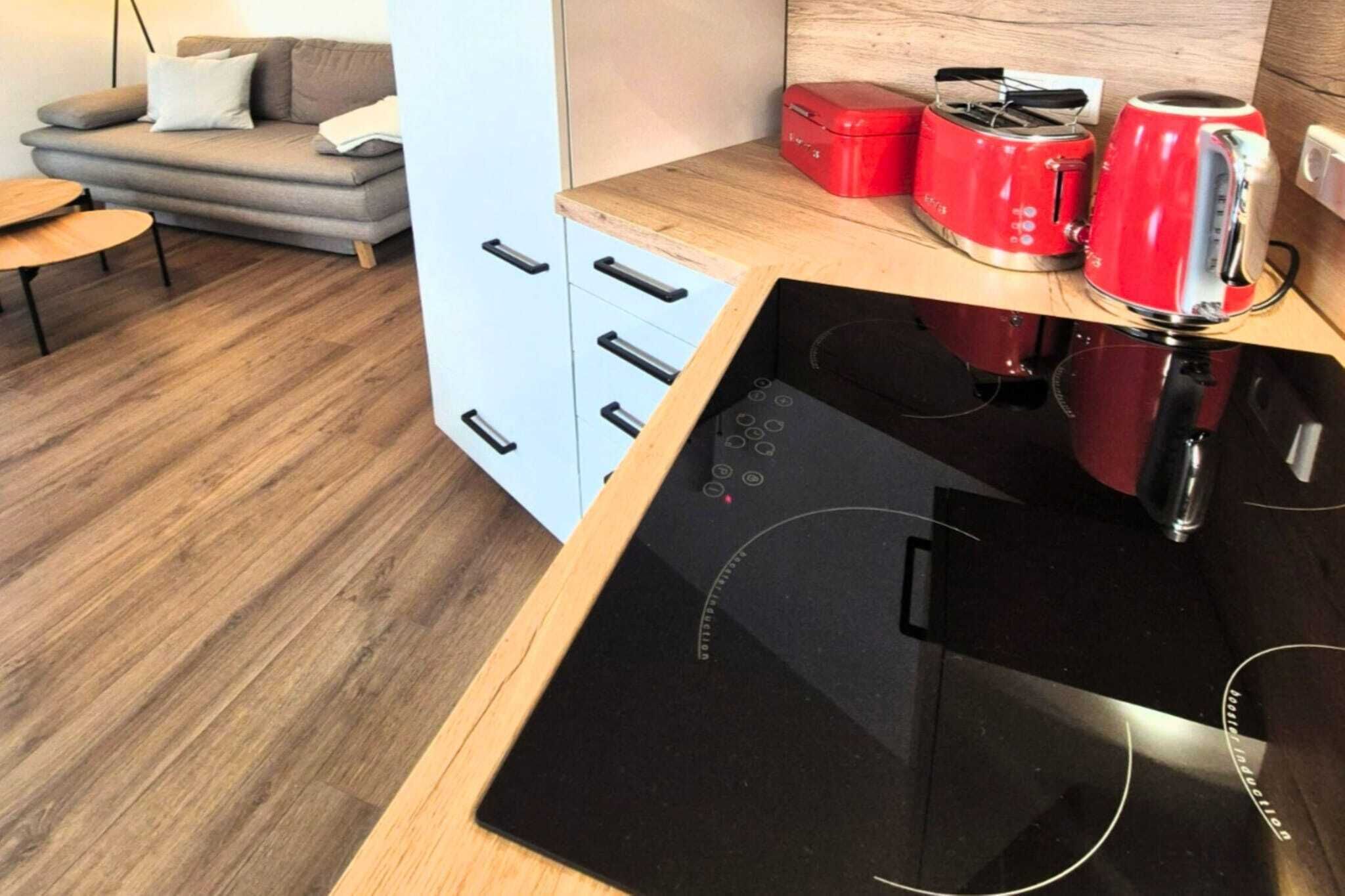 A modern kitchen with a black induction cooktop, a grey sofa, and a small wooden table.
