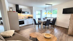 A modern kitchen with white cabinets, a dining area with a wooden table and chairs, and a large window providing natural light. - Moderne Ferienwohnung in Winterberg (Winterberg)