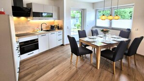 A modern kitchen with white cabinets, a black range hood, and a dining area with a wooden table and black chairs. - Moderne Ferienwohnung in Winterberg (Winterberg)