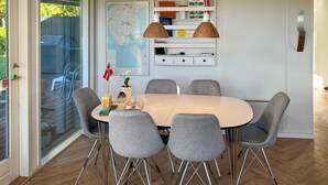 Ein Essbereich mit einem runden Tisch, sechs grauen Stühlen, zwei Pendelleuchten, einer Karte an der Wand und einer kleinen Pflanze.