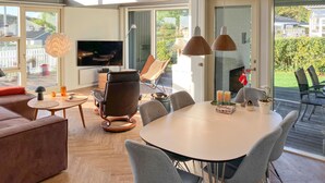 Ein modernes Wohnzimmer mit großem Fernseher, bequemen Sitzgelegenheiten und einem Essbereich mit Tisch und Stühlen.