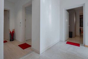 Een gang met witte wanden en een lichtgekleurde vloer, die leidt naar een kamer met een deur.