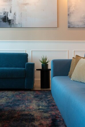 Een woonkamer met twee banken, een kamerkleed met patroon en een bijzettafeltje met een plant.