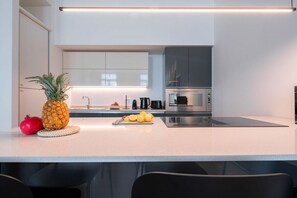 Een moderne keuken met een wit aanrecht, roestvrijstalen apparatuur en een granaatappel.