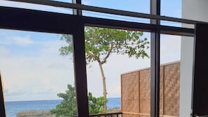 Une pièce avec une terrasse en bois, une vue sur la mer et une petite table agrémentée d’un coussin bleu.