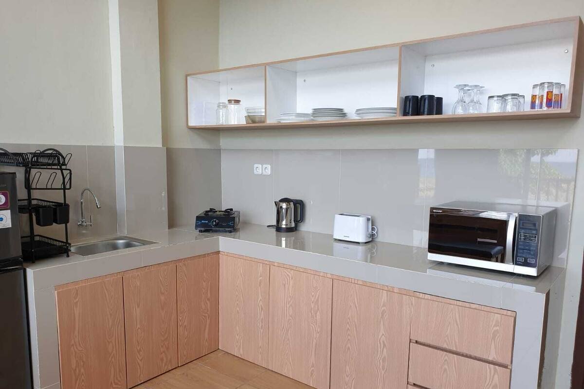 A modern kitchen with a built-in microwave, toaster, and kettle. There are wooden cabinets and a stainless steel sink.