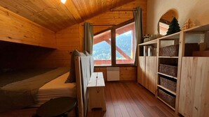 Une cabane en bois avec un lit en mezzanine, une petite table et une fenêtre donnant sur les montagnes.