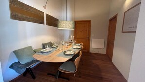 Un espace repas avec une table en bois dressée pour quatre personnes, entourée de chaises, d’un banc et d’un luminaire suspendu.