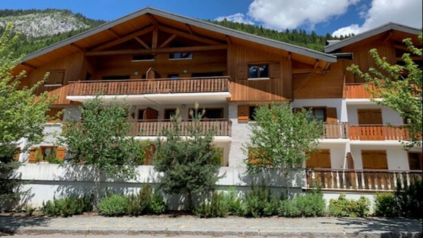 Un chalet en bois doté de plusieurs balcons, d’une façade en pierre et surplombant un paysage montagneux.