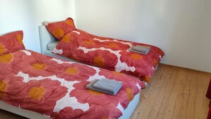 Deux lits simples avec une literie à motifs floraux, un plancher en bois et un rideau rouge.