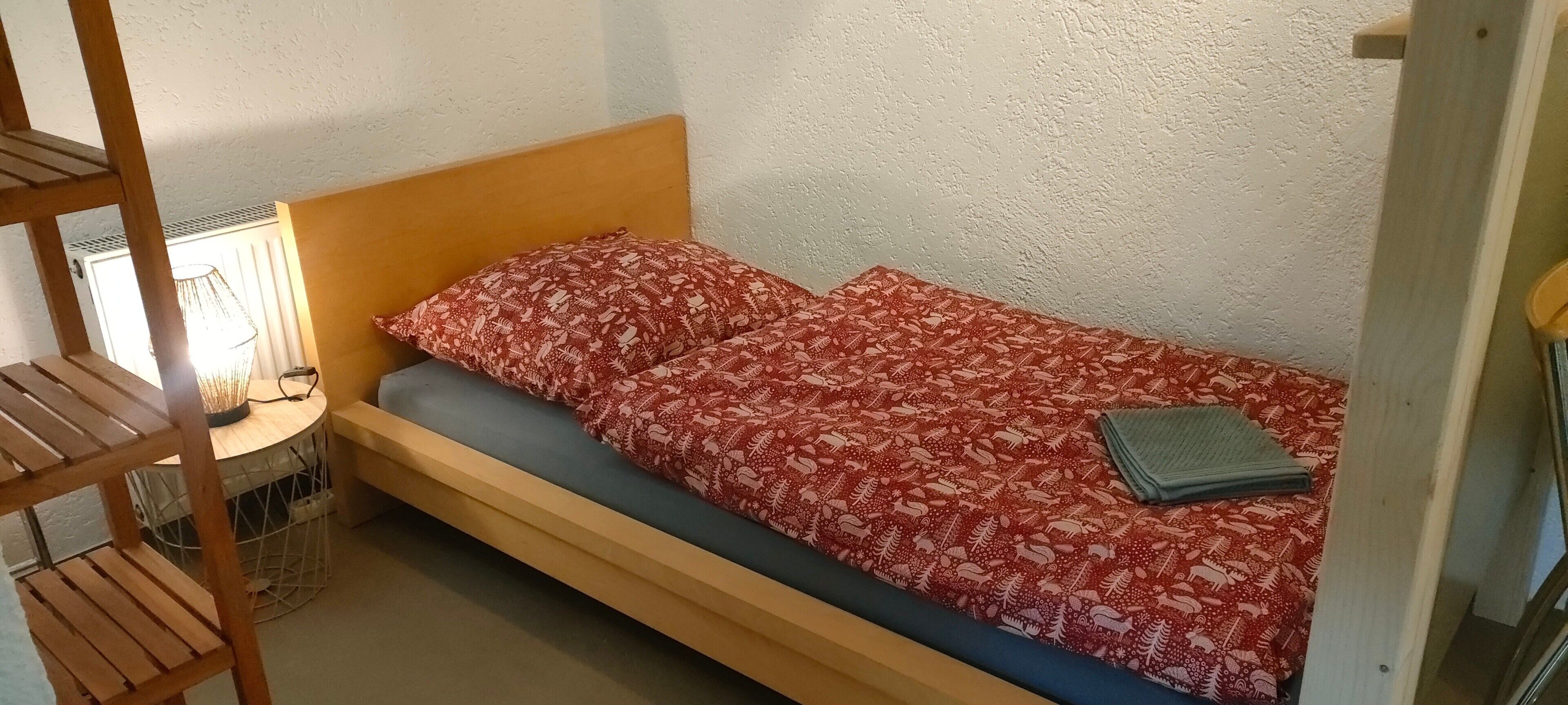 A single bed with a patterned bedspread, a wooden headboard, and a small bedside table with a lamp.