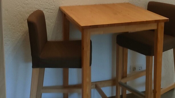 A small wooden table with two chairs, a framed picture on the wall, and a plain white wall. - Apartment 'Peter 2' with Private Terrace and Wi-Fi (Hessen - Michelstadt)