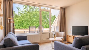 Een moderne woonkamer met een groot raam, een flatscreen-televisie en een eethoek.