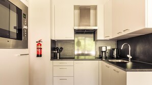 Een moderne keuken met witte kasten, een RVS magnetron, een gasafzuigkap, een koffiezetapparaat en een brandblusser.
