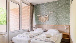 Een hotelkamer met twee bedden, een raam met uitzicht op een bakstenen muur, en een macramé decoratie aan de muur.
