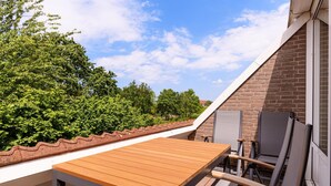 Een houten tafel en stoelen buiten op een terrasdak, met een bakstenen muur en uitzicht op bomen.