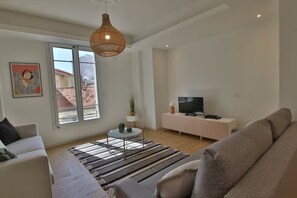 A modern living room with a sofa, a TV, a small table with a plant, and a large window.