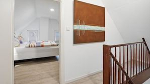 Un dormitorio con cama, suelo de madera, pared blanca y una escalera con barandilla de madera.