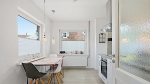 Una cocina compacta con comedor, una ventana con persianas, un radiador y una estufa.