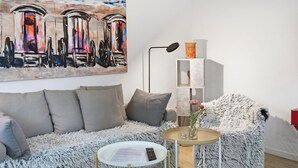 Una sala de estar moderna con un sofá, una mesa redonda con un florero, una lámpara y un cuadro en la pared.