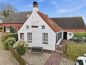 A white house with a red roof, a small porch, and a gravel driveway.