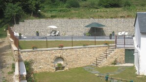 Un espace extérieur entouré de murs en pierre, agrémenté d’une arche en pierre, d’une terrasse pavée et d’un mur en pierre sur lequel s’étend un petit jardin.