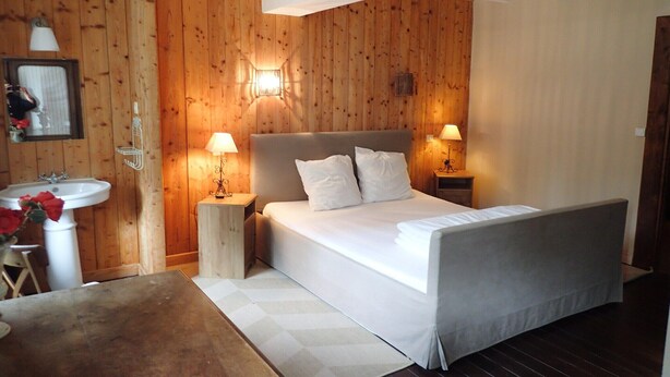 Une chambre avec un mur en bois, un lit avec une literie blanche, deux lampes de chevet, une table de chevet, une petite table et un lavabo avec un miroir.