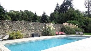 Une piscine rectangulaire avec un mur en pierre et des plantes en arrière-plan.