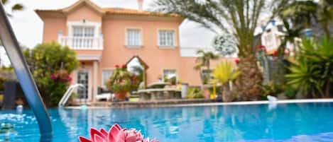Una piscina con decoración de flor de loto, un edificio con balcón y palmeras al fondo.