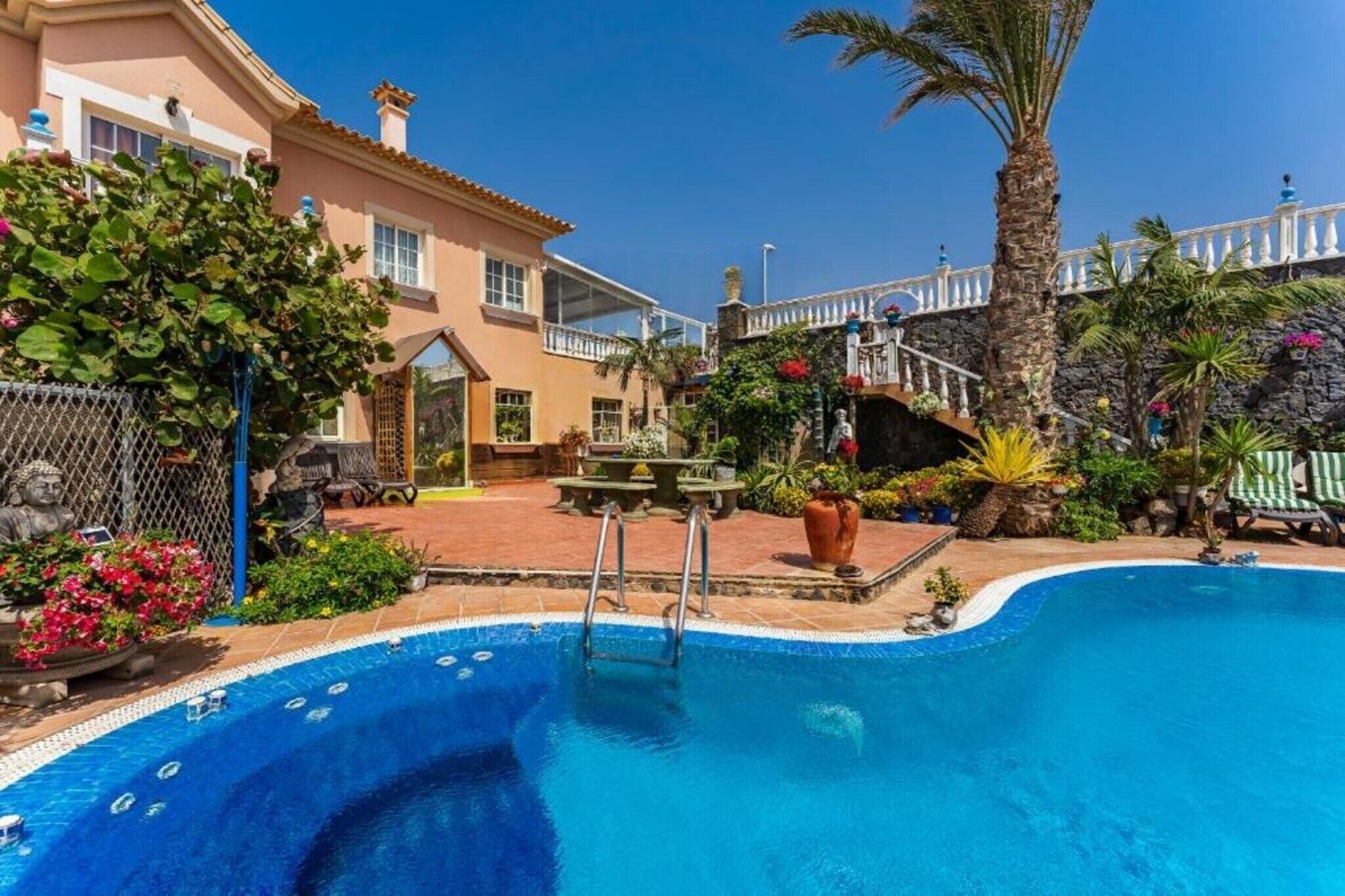 A swimming pool with a stone wall, a palm tree, and a building with a balcony.