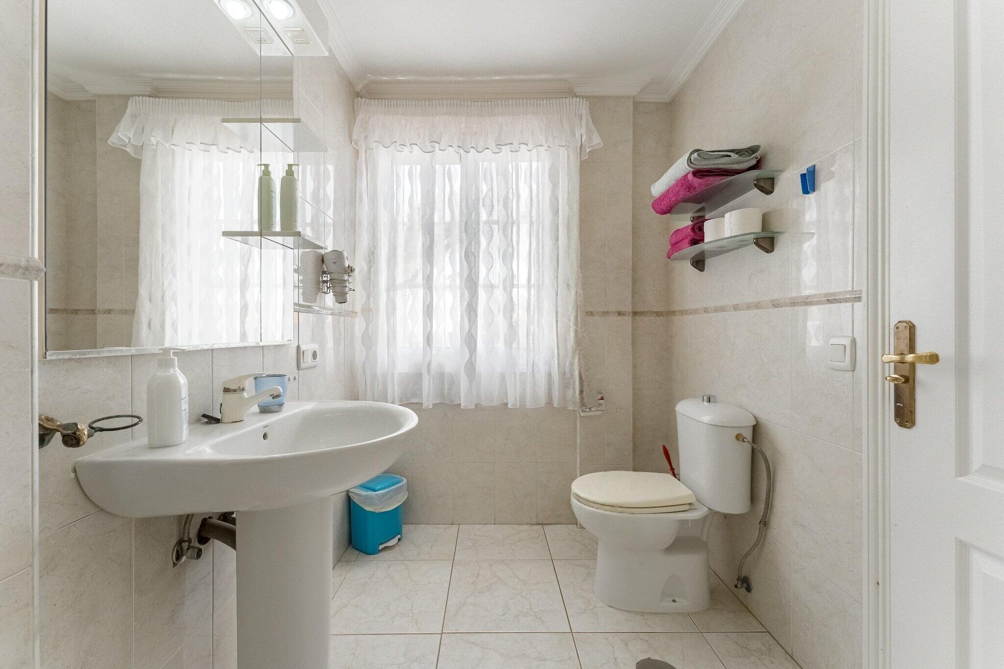 Un baño con lavamanos, inodoro y ventana con cortina.