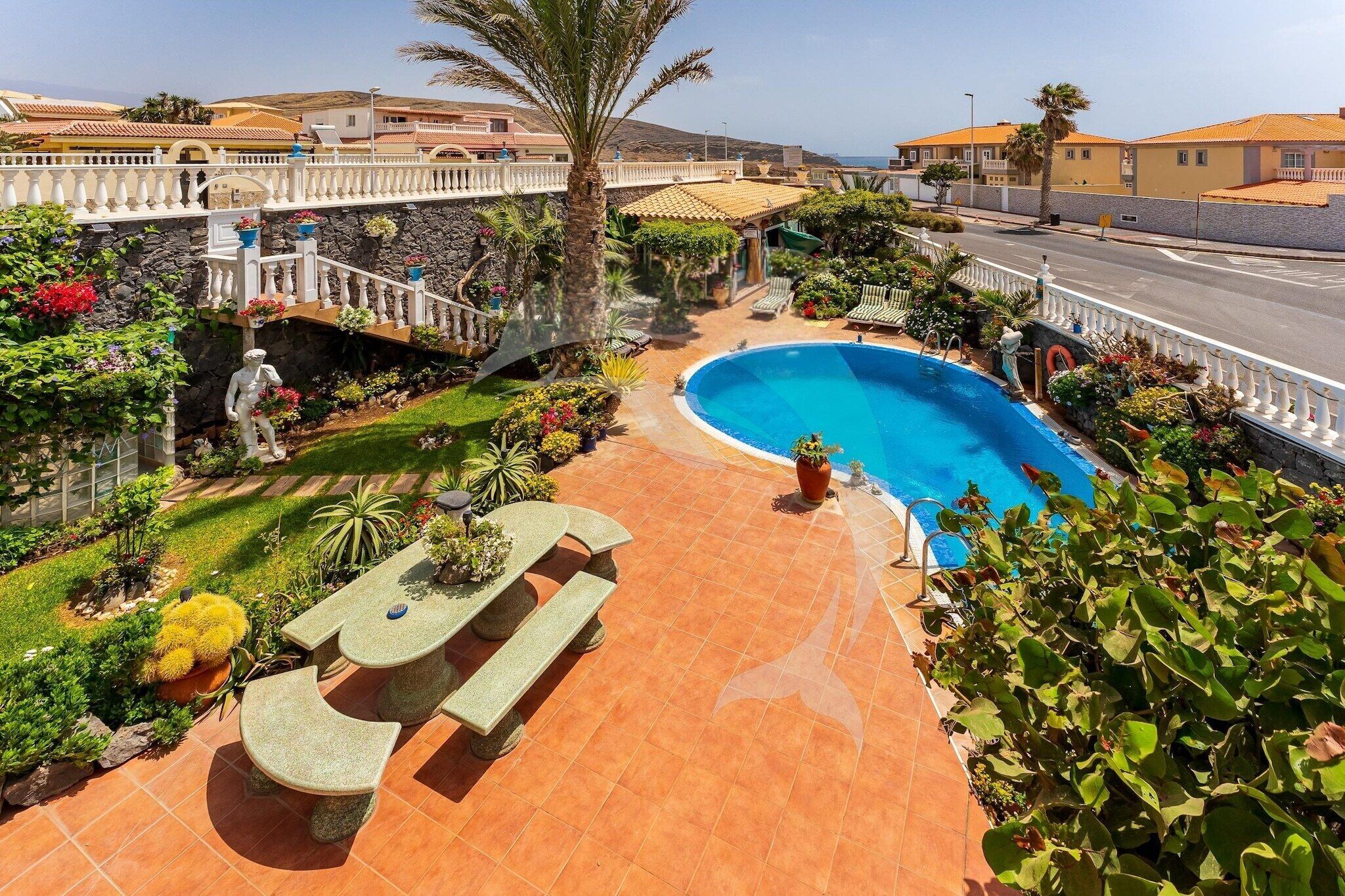 A swimming pool surrounded by a garden with a stone bench and a statue.