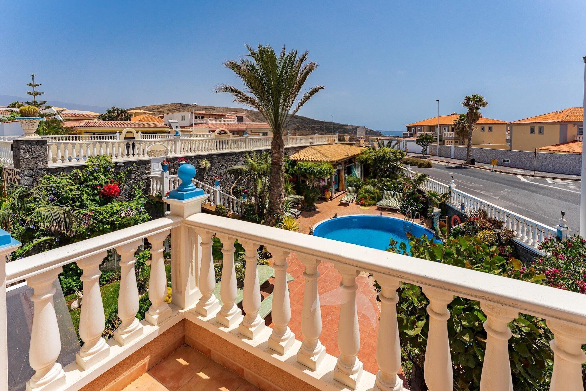 A balcony with a pool, surrounded by lush greenery and a view of the sea.
