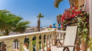 A balcony with a white chair, a view of the sea, and a flower wall. - Apartment overlooking heated pool (Santa Cruz de Tenerife)