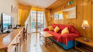 A cozy room with a wooden interior, a red sofa with yellow cushions, a wooden table, and a television on a wooden stand.