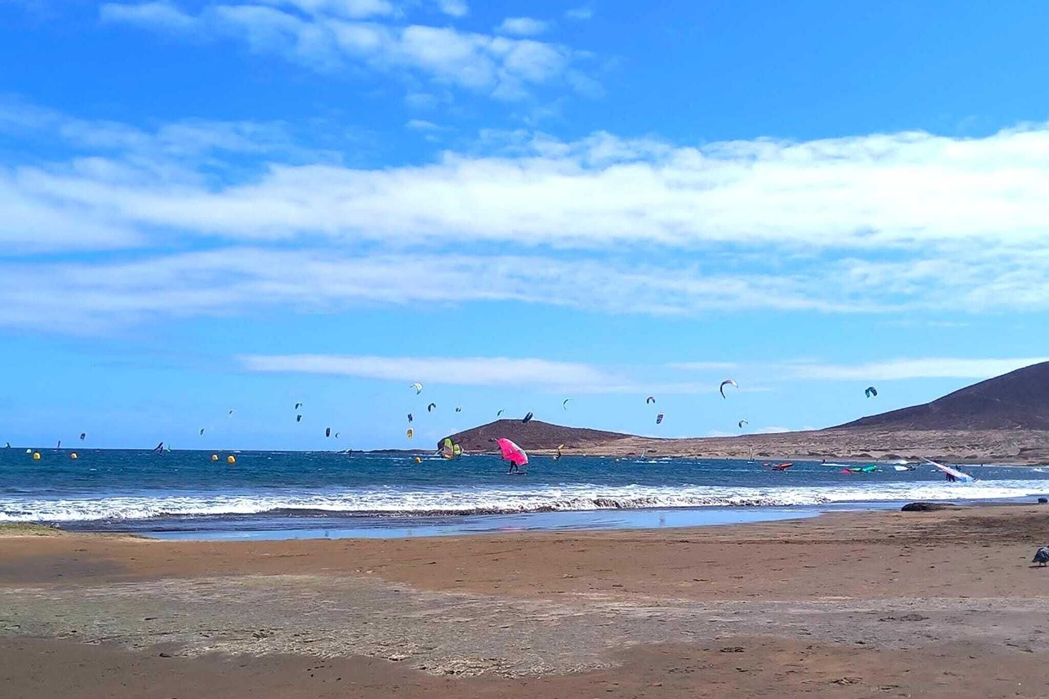 A beach with people flying kites and windsurfing.