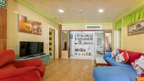 Ein Zimmer mit Fernseher, roten und blauen Sofas, einem Bücherregal und einer Tür zu einem weiteren Raum.