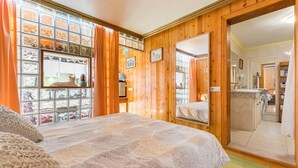 Ein Schlafzimmer mit einem großen Bett, Holzwänden, einem Fenster mit Vorhängen und einem Spiegel.