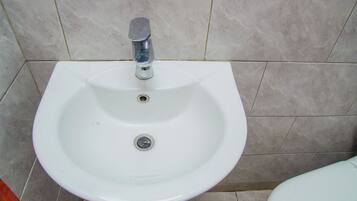 Uma pia branca assentada sobre pedestal, com uma única torneira, num banheiro com paredes e chão revestidos de azulejos.