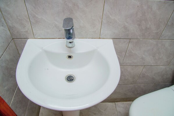 A white pedestal sink with a single faucet in a bathroom with tiled walls and floor.