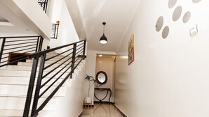 Un pasillo con una escalera, un espejo redondo y un aplique de pared.