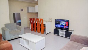 Una sala de estar con sofá, una mesa de centro, televisor y una cocina al fondo.
