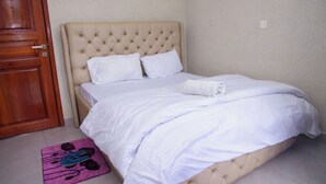 Una cama bien hecha con sábanas blancas, un cabecero capitonado y una alfombra rosa con estampado floral.