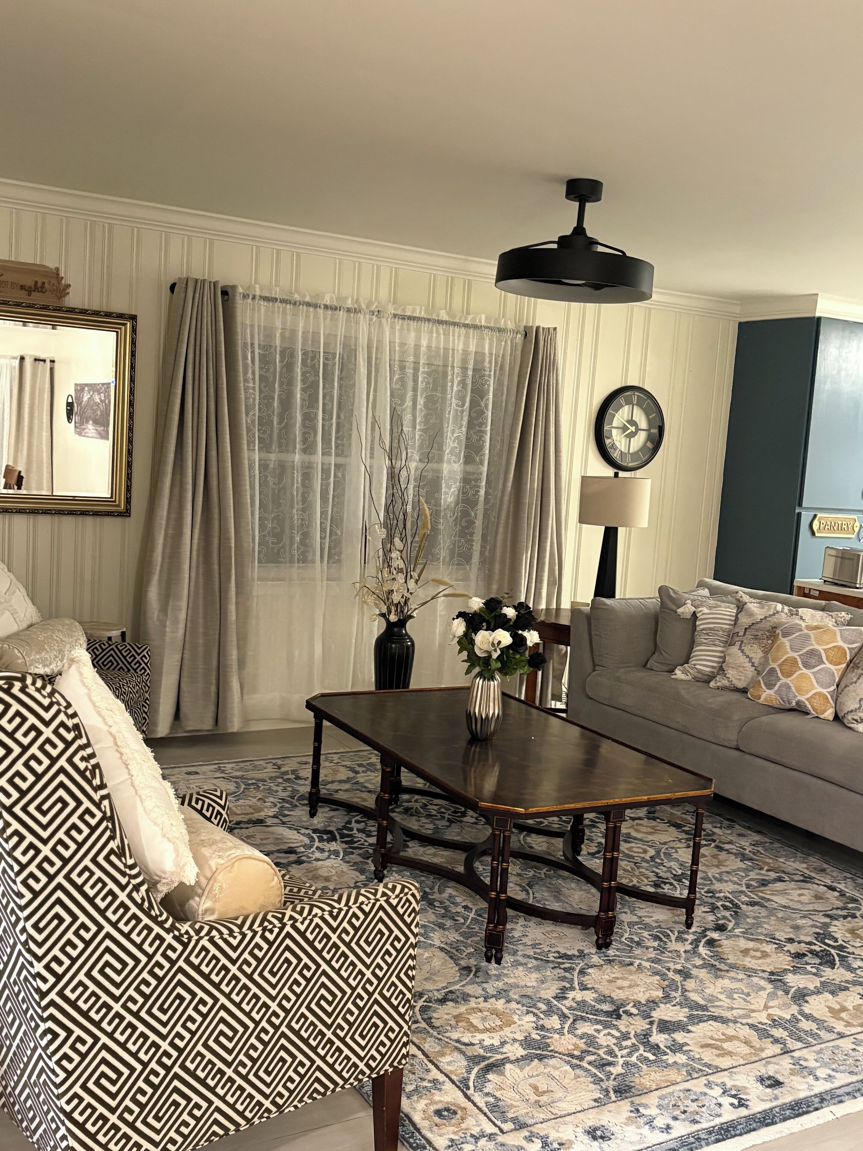 Un salon avec un canapé, un fauteuil, une table basse et une horloge au mur.