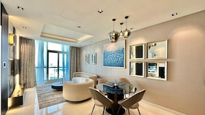 A modern living room with a round glass table, beige sofas, and a large window with curtains.