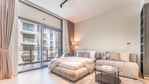 A modern bedroom with a large bed, a sofa, a coffee table, and a balcony with a view of buildings. - Studio Near Ras Al Khor Wildlife Sanctuary with Partial Creek Views (Dubai)