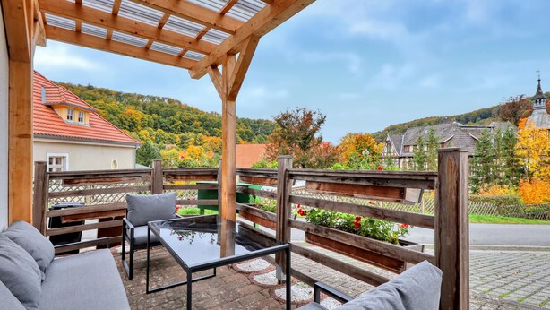 Un espace extérieur aménagé avec une pergola, une clôture en bois et une vue sur un village avec ses maisons et son église.