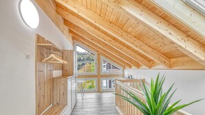 Interior de fusta amb sostre inclinat, parets de fusta i una finestra gran que ofereix vistes a la verdura exterior.