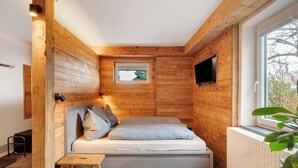 Une petite pièce chaleureuse, avec un lit, une petite table, une fenêtre et des murs en bois.